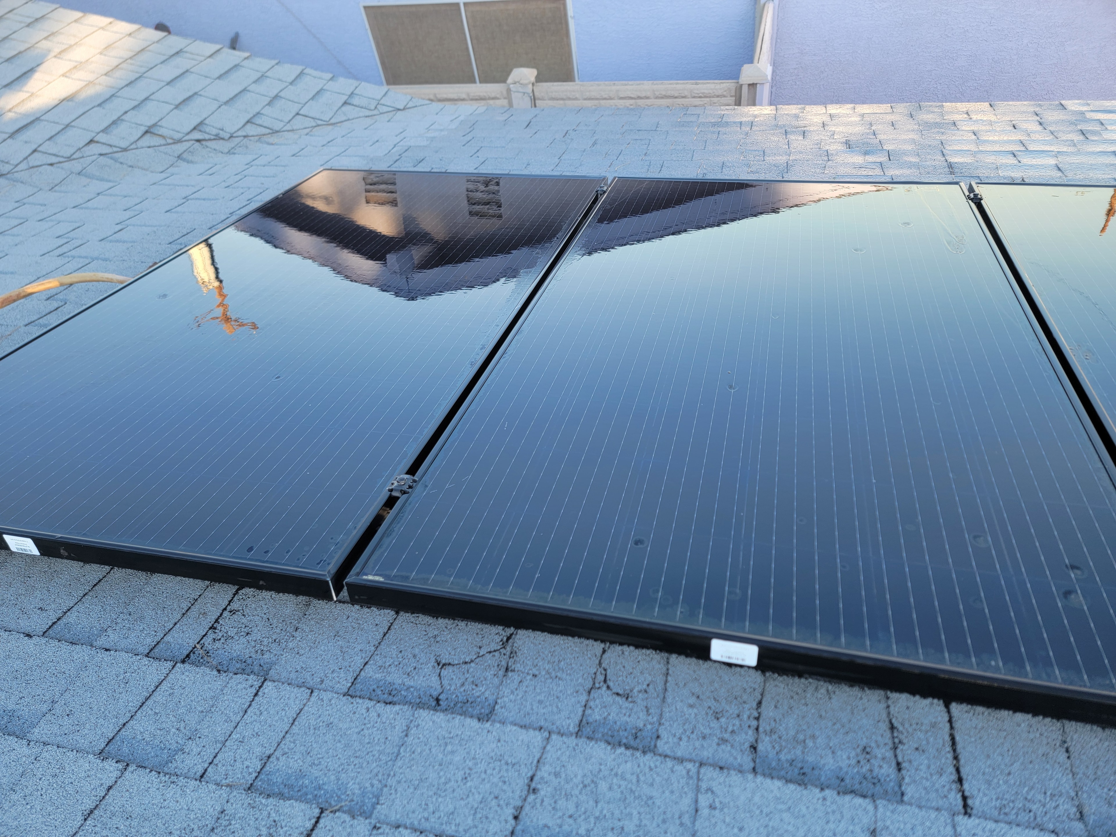 Freshly cleaned black solar panels reflecting sky on shingle roof