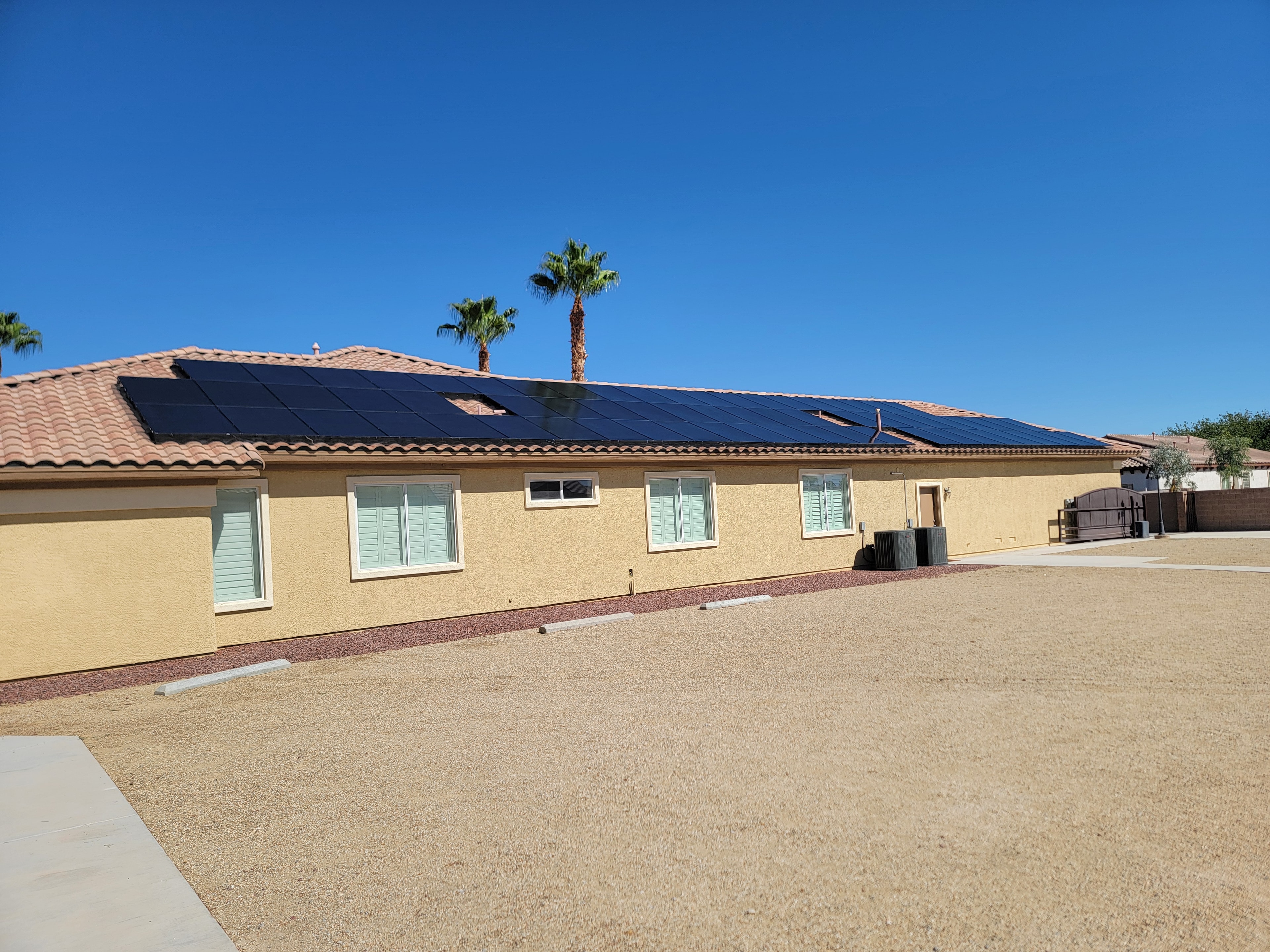 Freshly cleaned solar panels on large tile roof home with palm trees and blue sky